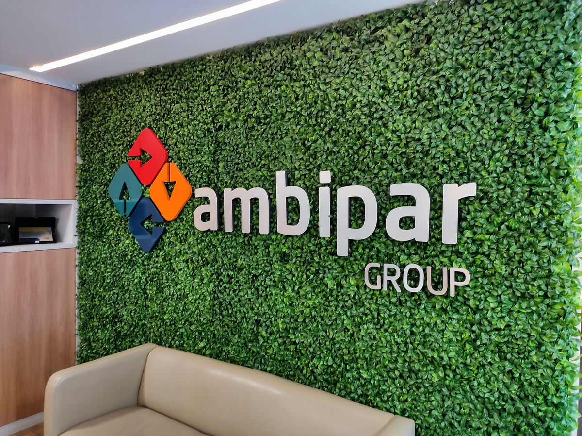 Logo e letras 3D em parede interna com folhagem artificial.