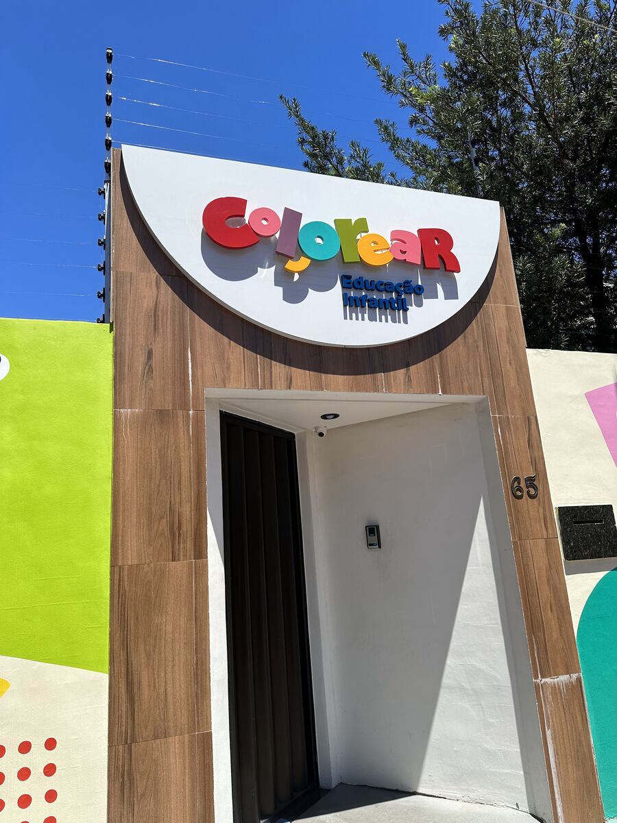 Fachada revestida com painéis em textura amadeirada e letreiro de letras caixa coloridas.