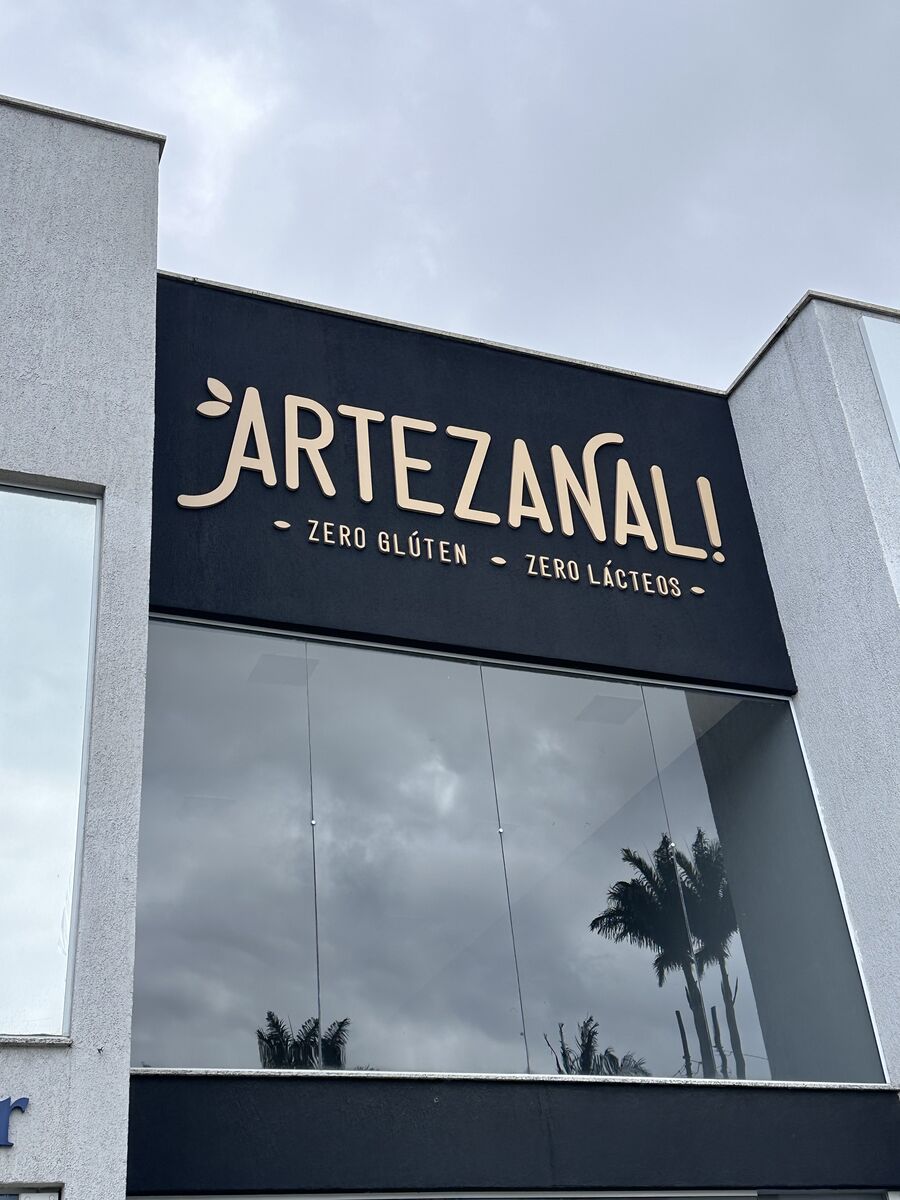Letreiro caixa preto com letras douradas da Artezanal em fachada comercial.