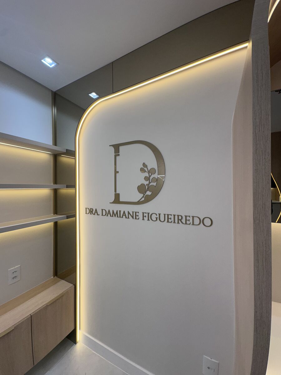 Letras em acrílico dourado aplicadas em parede interna de clínica, com iluminação de embutir.