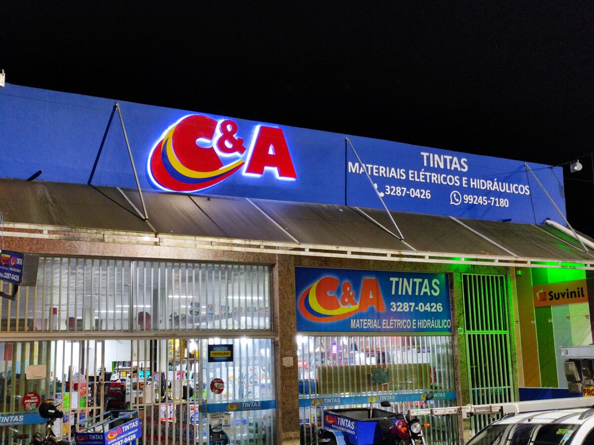 Loja com letreiros luminosos coloridos na fachada, exibindo nome e serviços.