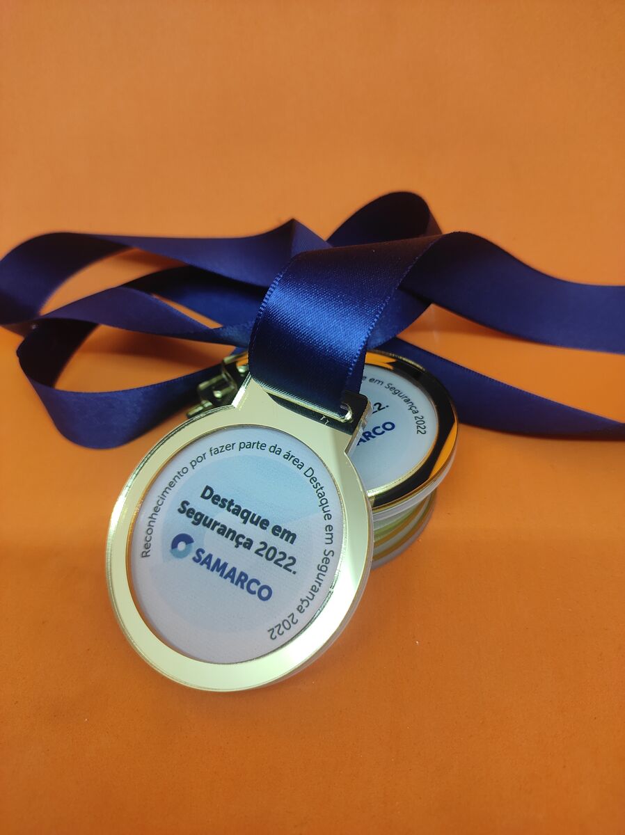 Medalha de reconhecimento dourada com fita azul para premiação corporativa.