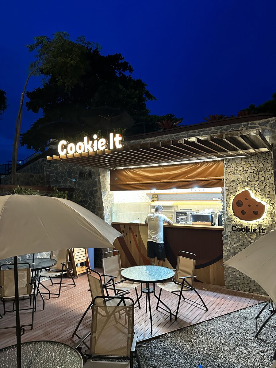 Letreiro luminoso em letras caixa e logo de cookies em fachada noturna.